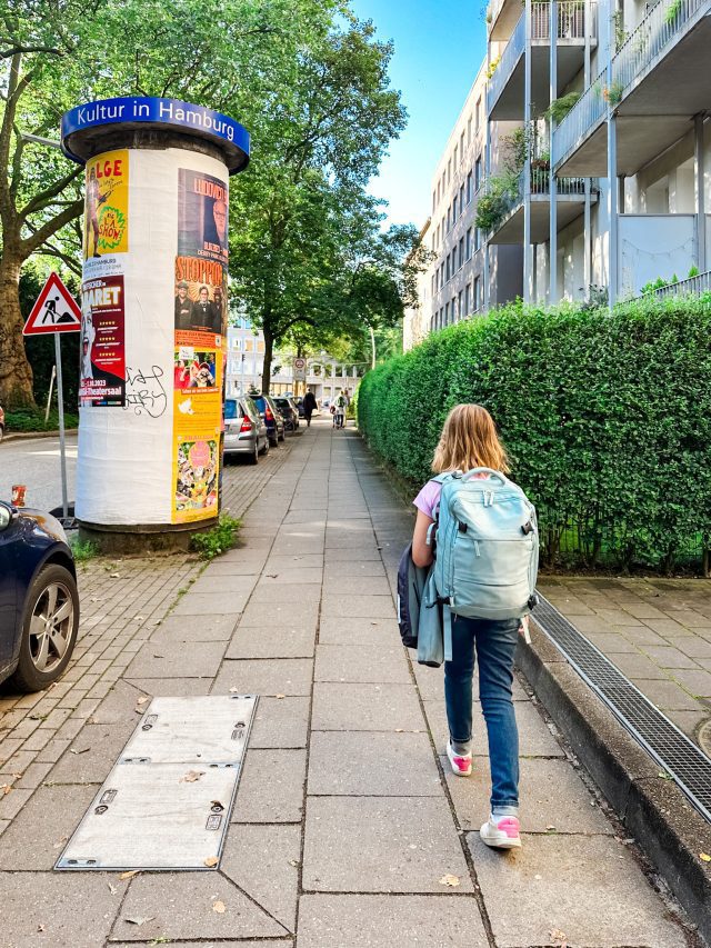 Girl walking on a Hamburg sidewalk wearing a travel backpack.