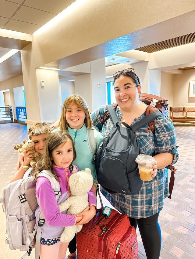 family with three kids and one mom wearing travel backpacks before a flight to europe